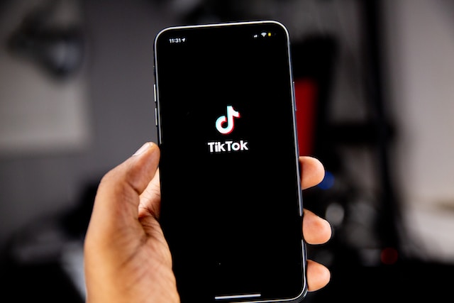One hand holds a smartphone with the TikTok logo on the screen.